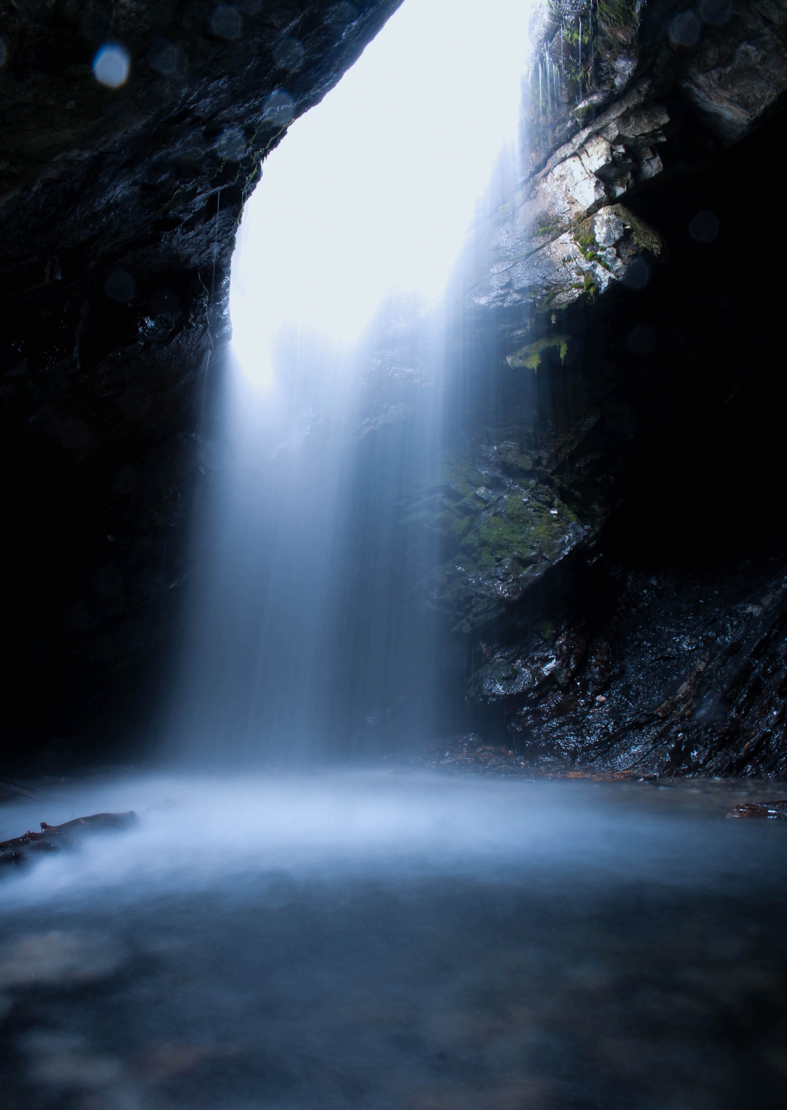 There is a waterfall coming out of a cave into a river (water, water resources, light, waterfall, watercourse)