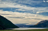 Lago de alta montaña sereno al atardecer con una majestuosa cordillera y nubes dramáticas