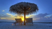 Tranquil Sunset Over Tropical Shoreline with Palm Umbrella and Lounge Chairs