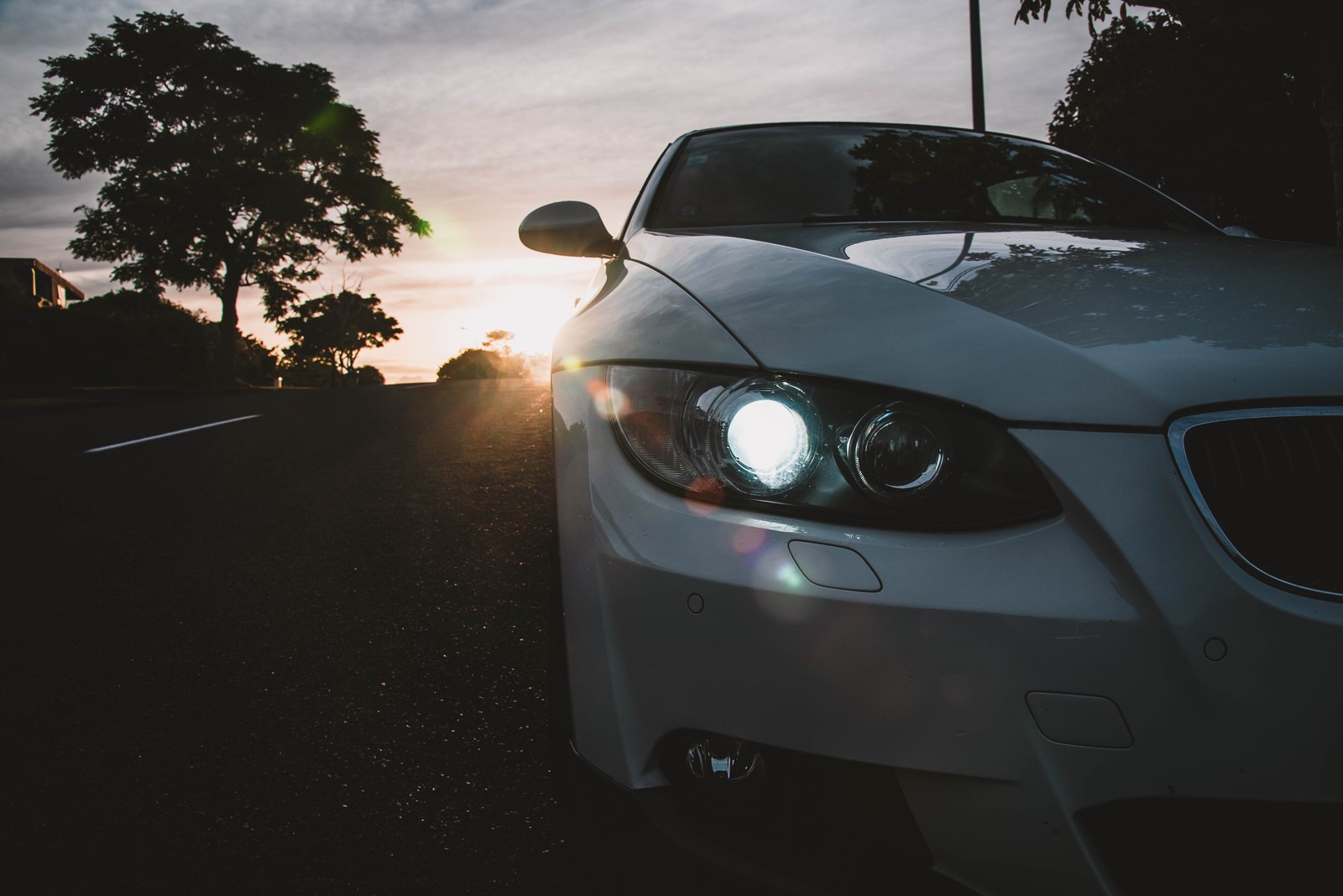 A close up of a car parked on a street with the sun setting (headlamp, automotive lighting, bmw, executive car, compact car)