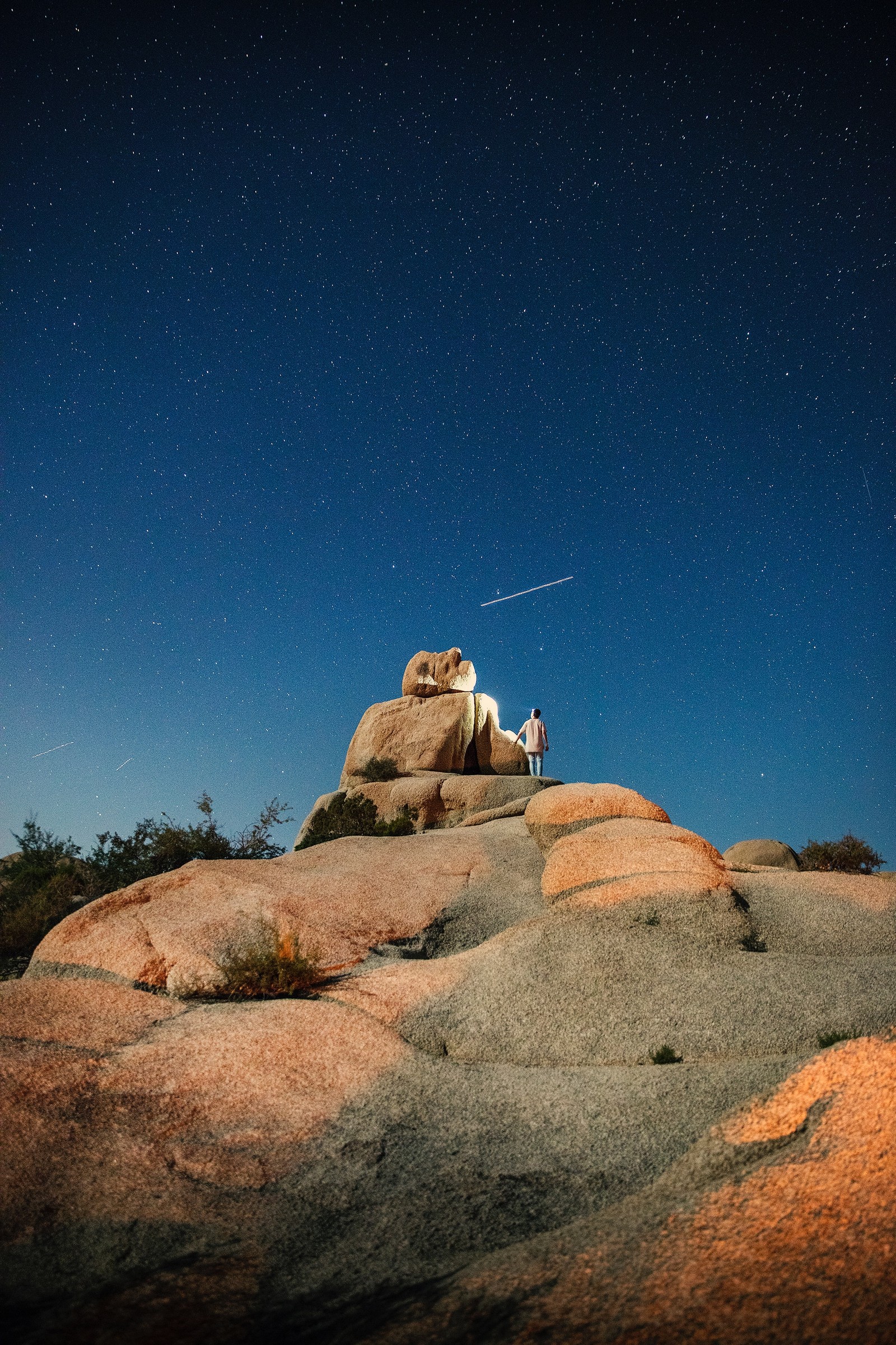 There is a man standing on a rock with a plane flying overhead (rock, star, night, astronomical object, landscape)