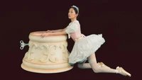 Irene from Red Velvet elegantly poses in a whimsical ballet-inspired outfit, interacting with a decorative, oversized music box.