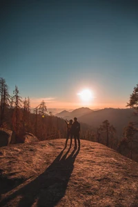 Figuras en silueta abrazando el amanecer en medio de un sereno paisaje montañoso.