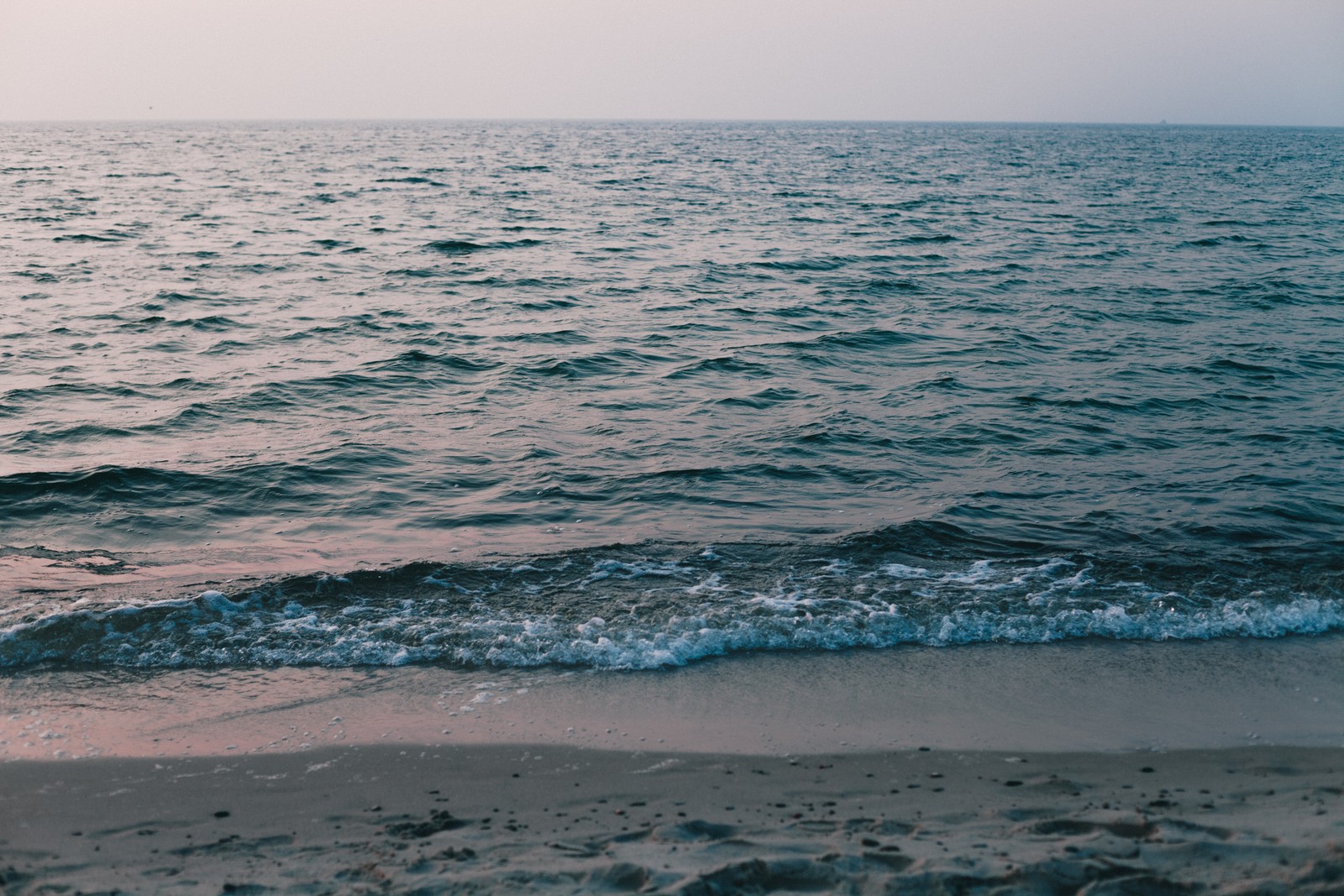 Eine person steht am strand mit einem surfbrett (meer, ozean, ostsee, strand, wasser)