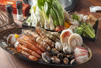 Un assortiment vibrant de fruits de mer et de légumes frais disposés sur un plateau, mettant en valeur une variété de crevettes, de palourdes, de coquilles Saint-Jacques et de légumes verts, parfait pour un repas inspiré de la cuisine thaïlandaise.