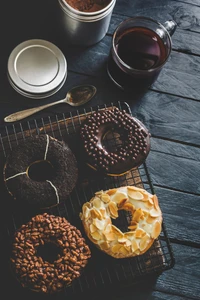 Donuts gourmet sortidos em uma grade de resfriamento, acompanhados por uma xícara de café, exibindo uma variedade de coberturas e texturas.