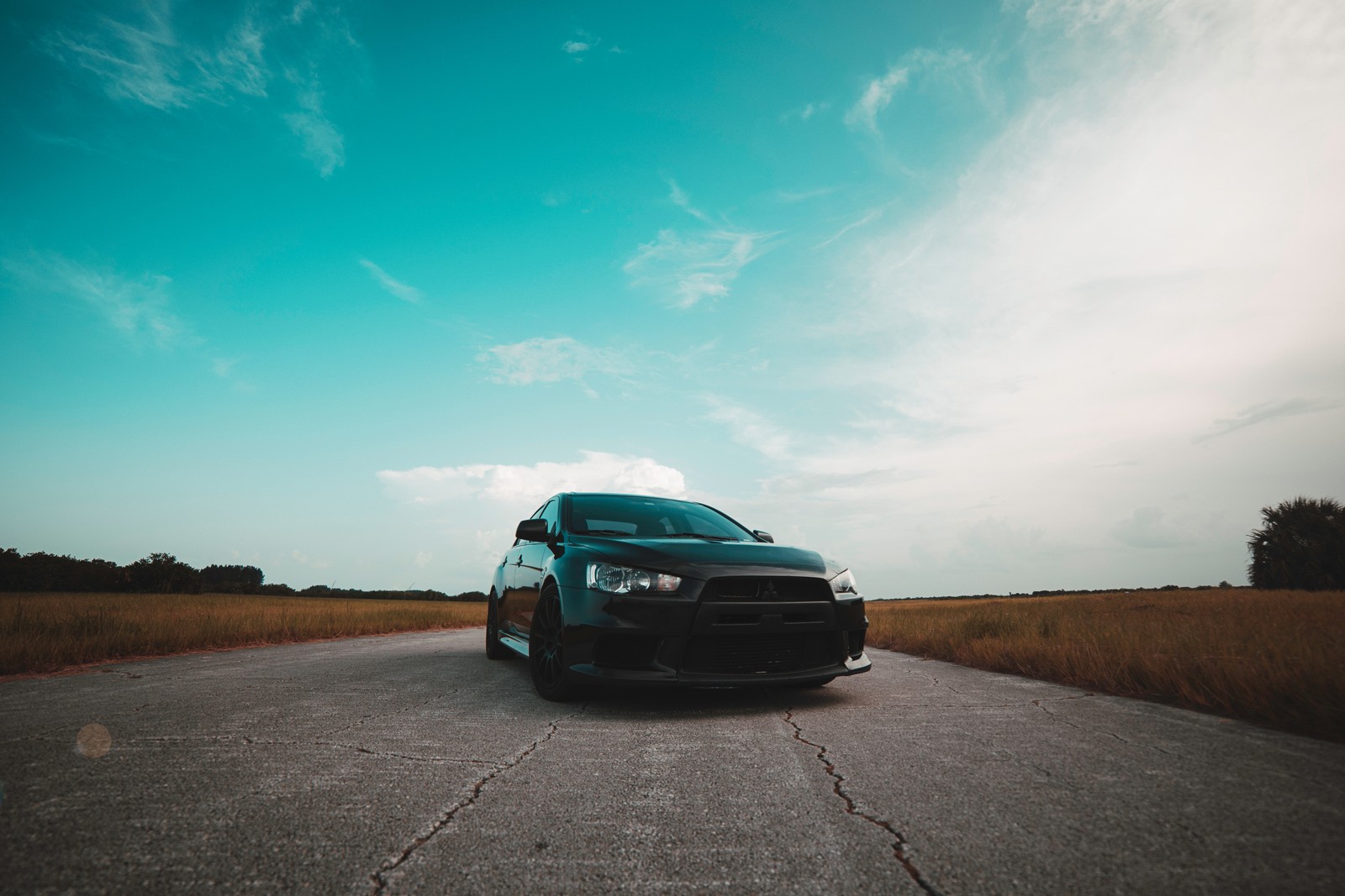 Um close-up de um carro estacionado em uma estrada perto de um campo (mitsubishi motors, mitsubishi lancer evolution, carro, mitsubishi, carro esportivo)