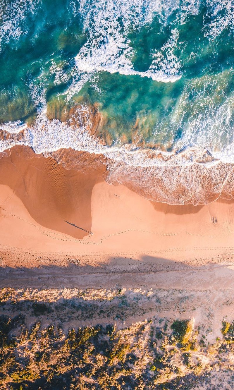 Vista aérea de una playa con una tabla de surf y una persona na areia (anime, negro, azul, coche, coches)