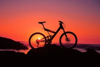 Silhouette d'un vélo contre un coucher de soleil vibrant sur une plage marocaine.