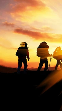 Siluetas de excursionistas contra un vibrante cielo anaranjado al atardecer.