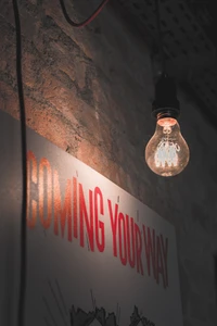 Vintage incandescent light bulb illuminating a wall with a bold graphic message.