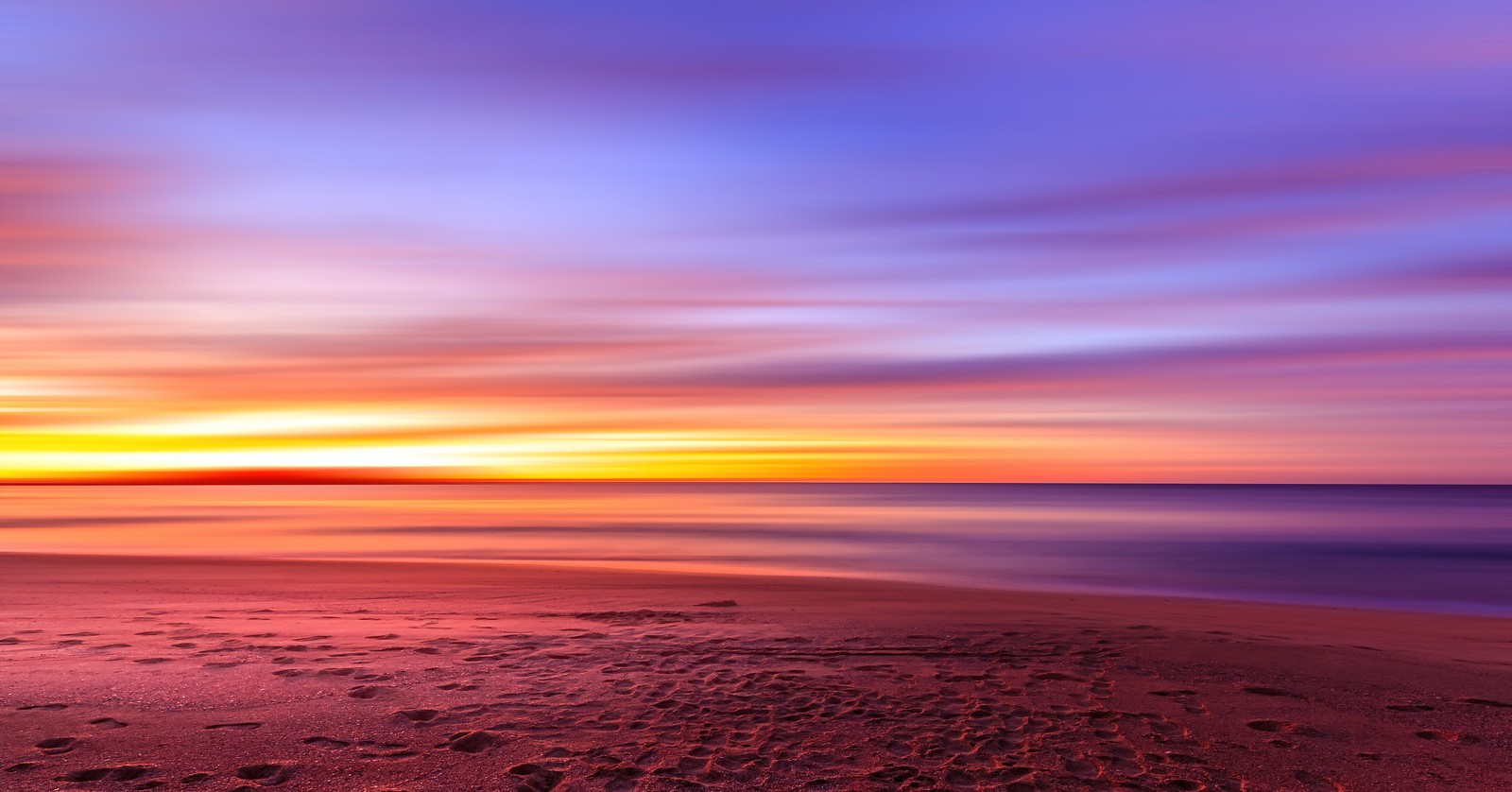 Vista do pôr do sol na praia com pegadas na areia (costa, por do sol, praia, exposição longa, crepúsculo)