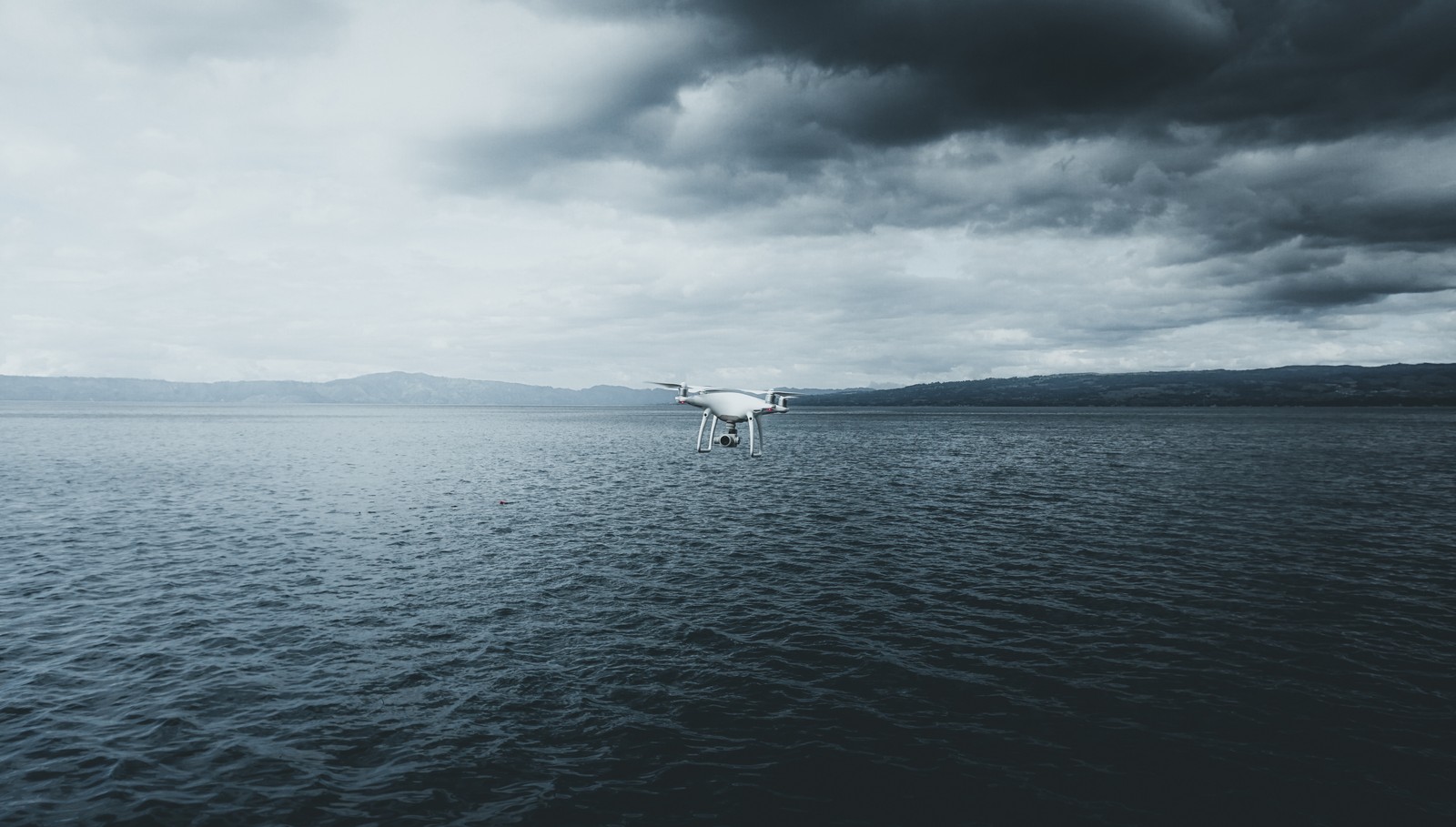 Il y a un petit bateau blanc flottant sur l'eau sous un ciel nuageux. (eau, mer, horizon, nuage, océan)