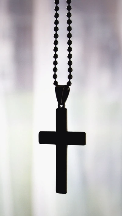 Silhouette of a cross pendant on a beaded necklace against a soft background.