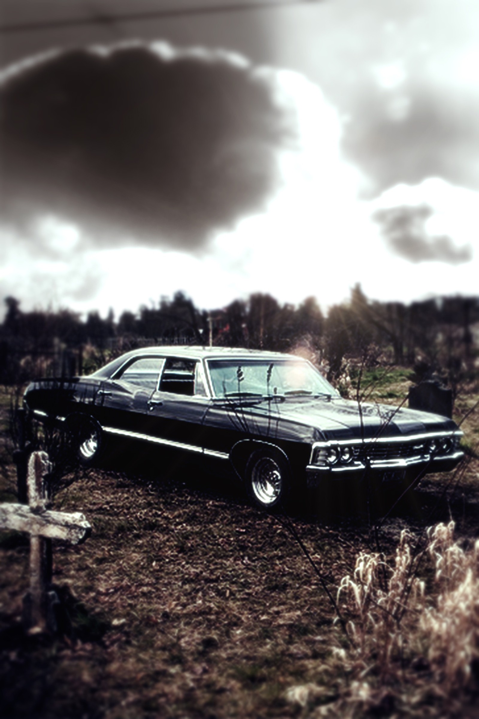 Une voiture noire garée dans un champ sous un ciel nuageux (dean, impala, sam, émission de télévision, winchester)