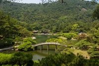 Jardim japonês sereno com uma ponte sobre águas tranquilas cercado por vegetação exuberante.