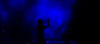 Silhouette d'un chanteur sur scène sous des lumières dramatiques bleues et violettes lors d'une performance de concert.