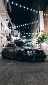 Sleek BMW M3 sports sedan parked under ambient city lights, showcasing its matte finish and aggressive stance.