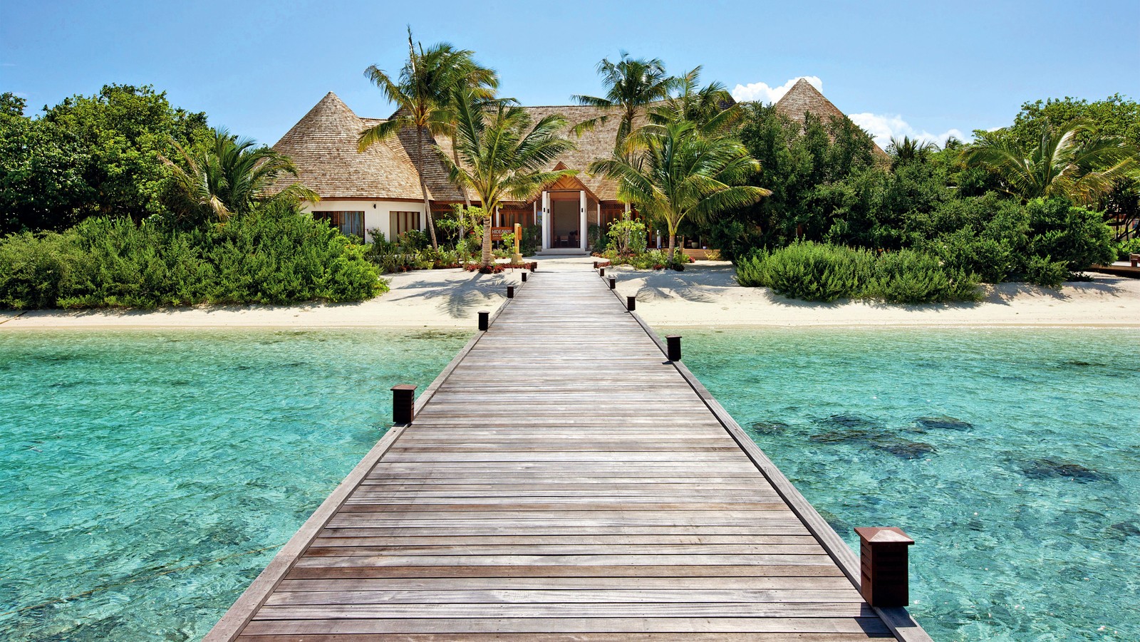 A wooden pier leading to a beach with a thatched house (resort, vacation, beach, tourism, seaside resort)