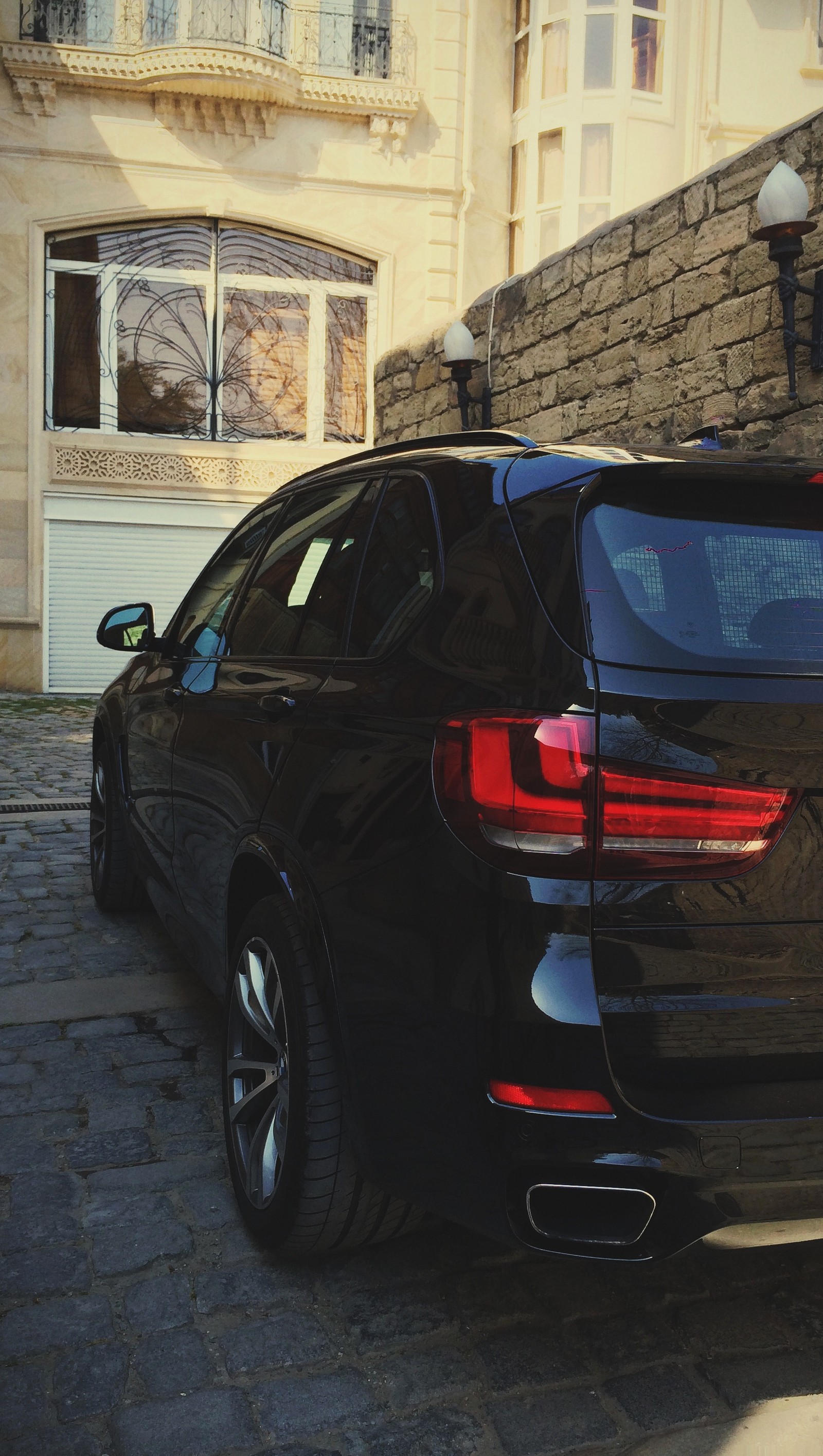 Bmw x5 geparkt auf einer kopfsteinpflasterstraße vor einem großen gebäude (baku, bmw, bmw m, autos, hd)