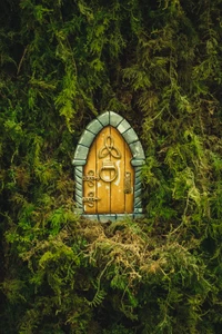 Whimsical fairy door nestled in lush green moss, blending art and nature in a serene landscape.