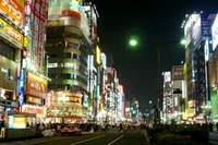 Cenário urbano noturno vibrante de Shinjuku, exibindo arranha-céus iluminados e uma vida urbana agitada.