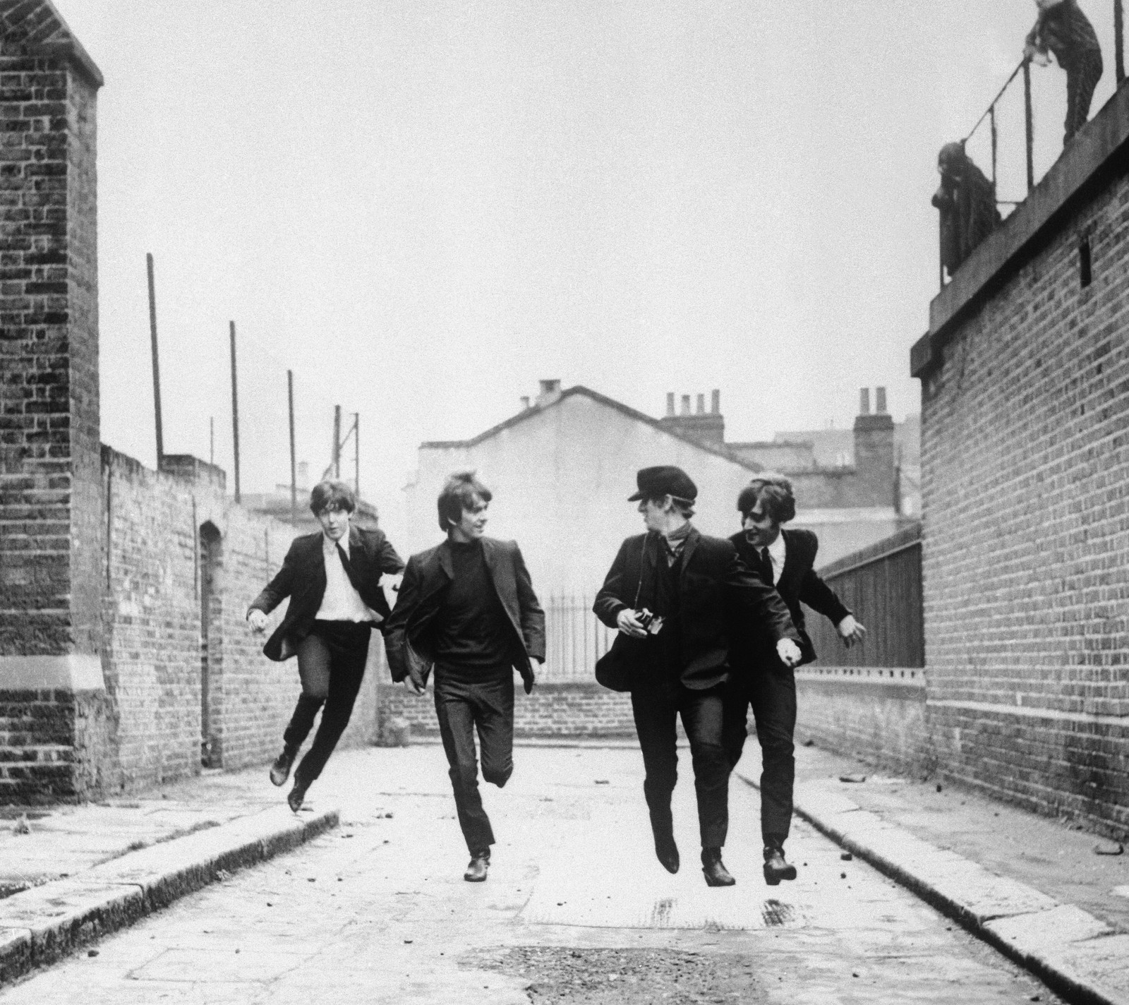 Arafed black and white photo of a group of men running down a street (paul, ringo, the beatles)