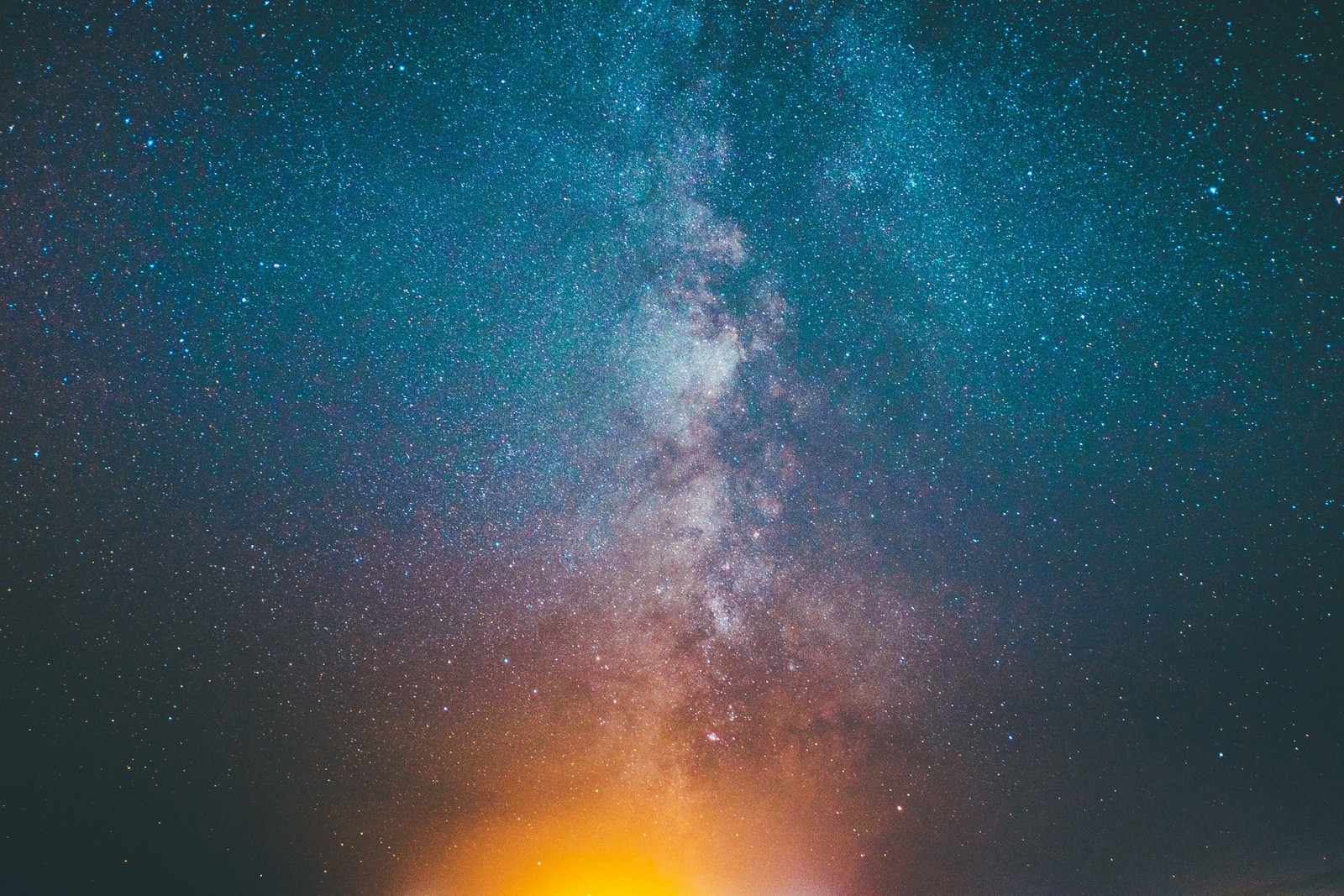 Una persona de pie en una playa bajo un cielo brillante con fuego (galaxia, cielo, estrellas, universo)