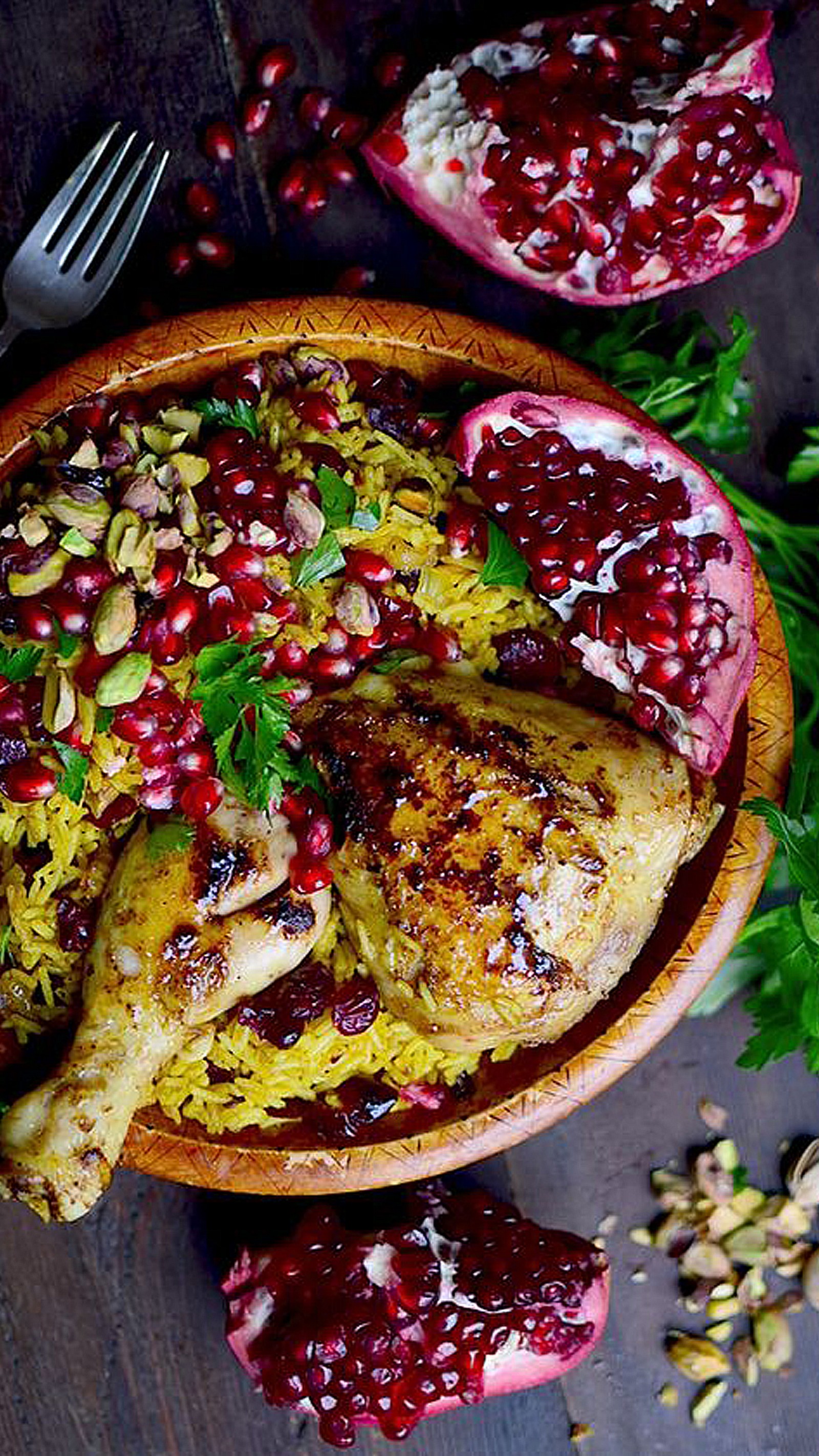 Un bol de nourriture avec une fourchette et quelques grenades (poulet, nourriture, vert, rouge, riz)