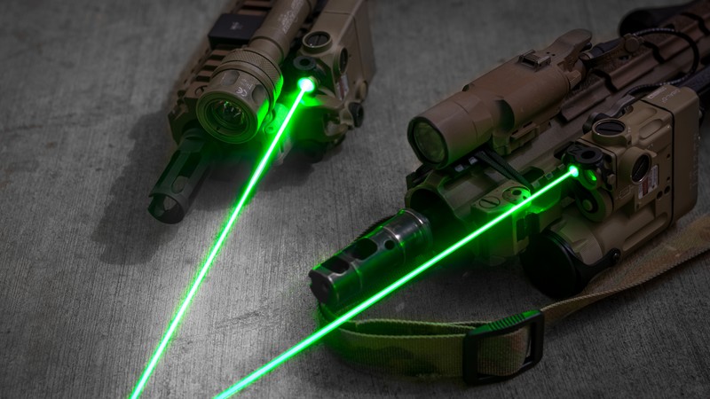 Two laser guns with green lights on a table (weapon, gun, sight, green, light)