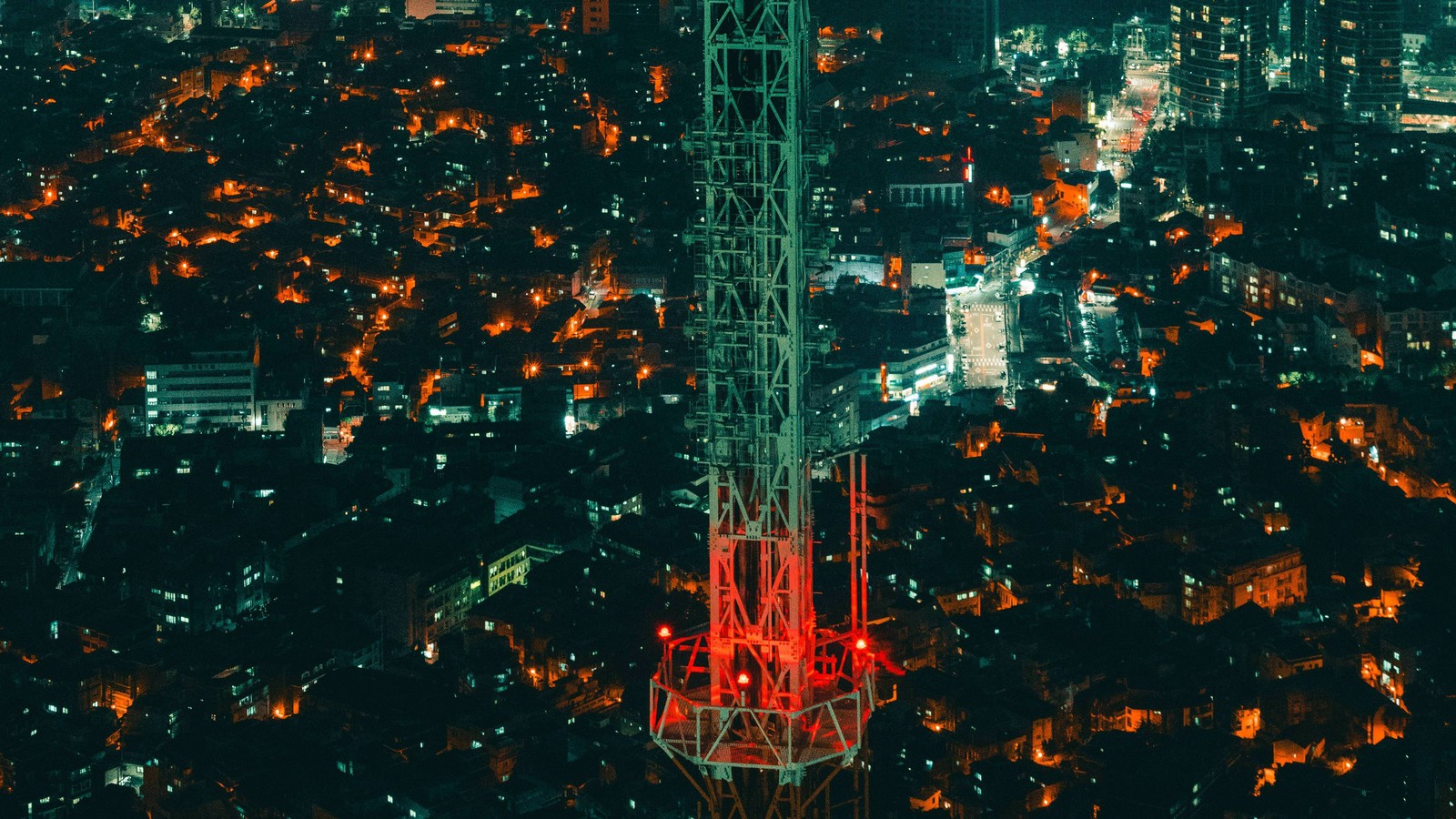 Uma vista de uma cidade à noite com uma torre em primeiro plano (metrópole, cidade, área urbana, assentamento humano, paisagem urbana)