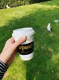 Segurando uma xícara de café em um gramado verdejante com um pássaro ao fundo