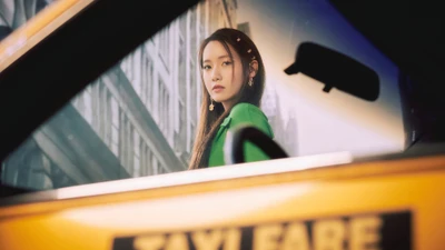 Yoona dans une tenue verte frappante, encadrée par le taxi jaune emblématique, dégageant élégance et confiance sur fond de ville.