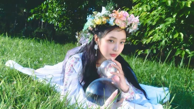 Joy do Red Velvet em um cenário de jardim fantasioso, segurando orbes de cristal, vestida com um traje floral e uma coroa de flores.