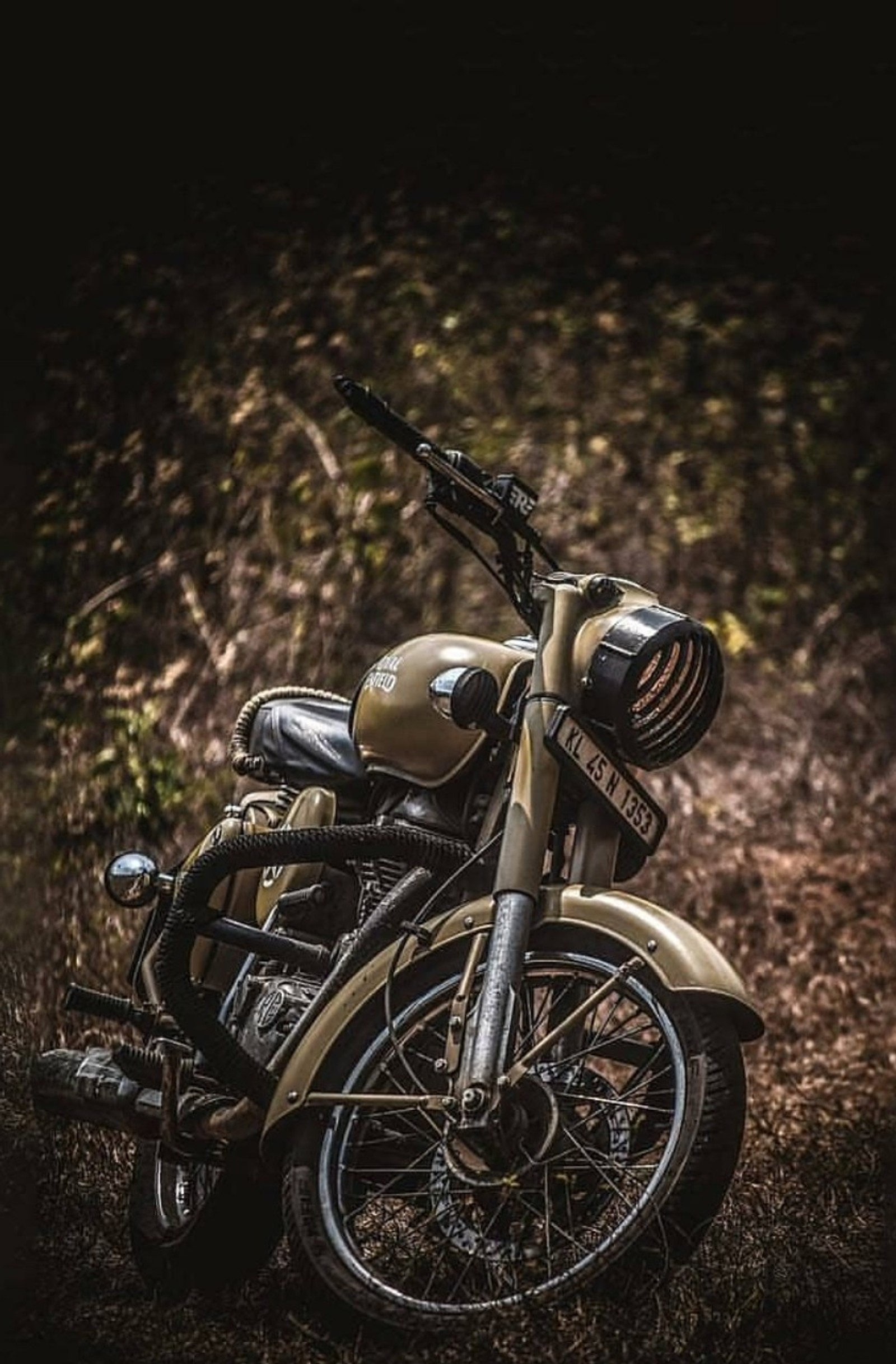 Um close de uma motocicleta estacionada em um campo perto de uma floresta (royal enfield, clássico 500, classic 350, harley davidson, duque)