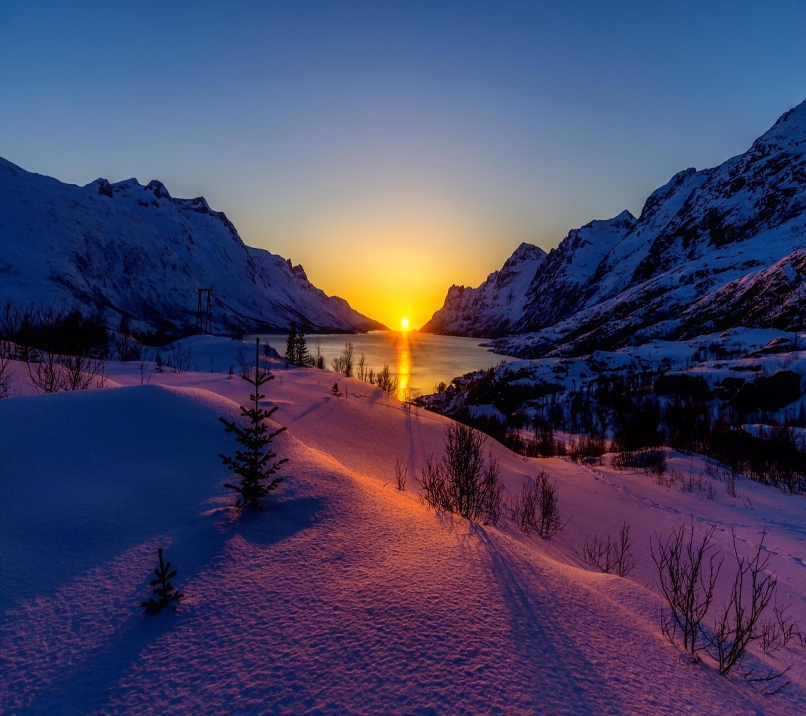 Una vista de un atardecer sobre una cordillera nevada con un lago (hermoso, lindo, mirada, agradable)