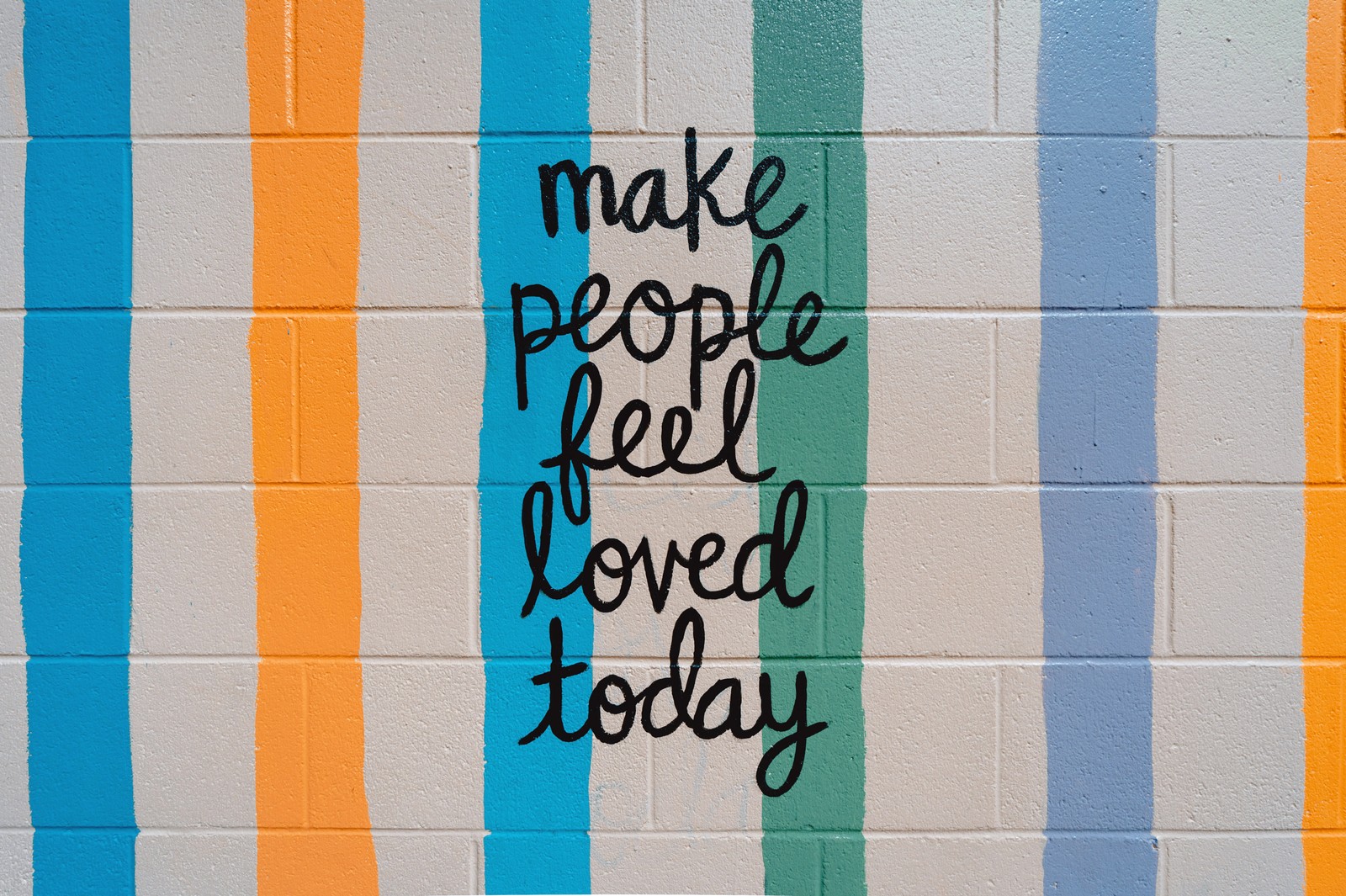 Graffiti sur un mur avec un message qui dit de faire sentir les gens aimés aujourd'hui (make people feel, love today, citations populaires, mur en briques, rayures)