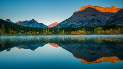 Lago de alta montaña sereno que refleja montañas majestuosas y árboles otoñales