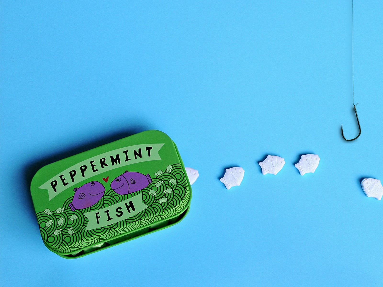 There is a tin of peppermint fish next to a fishing hook (green, sky, design, font)