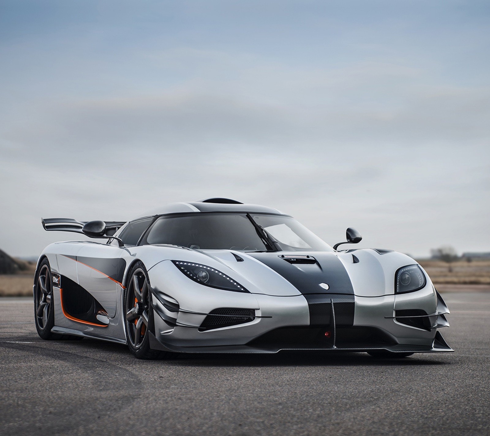 A close up of a silver and orange sports car on a road (and, koenigsegg, silver, white)