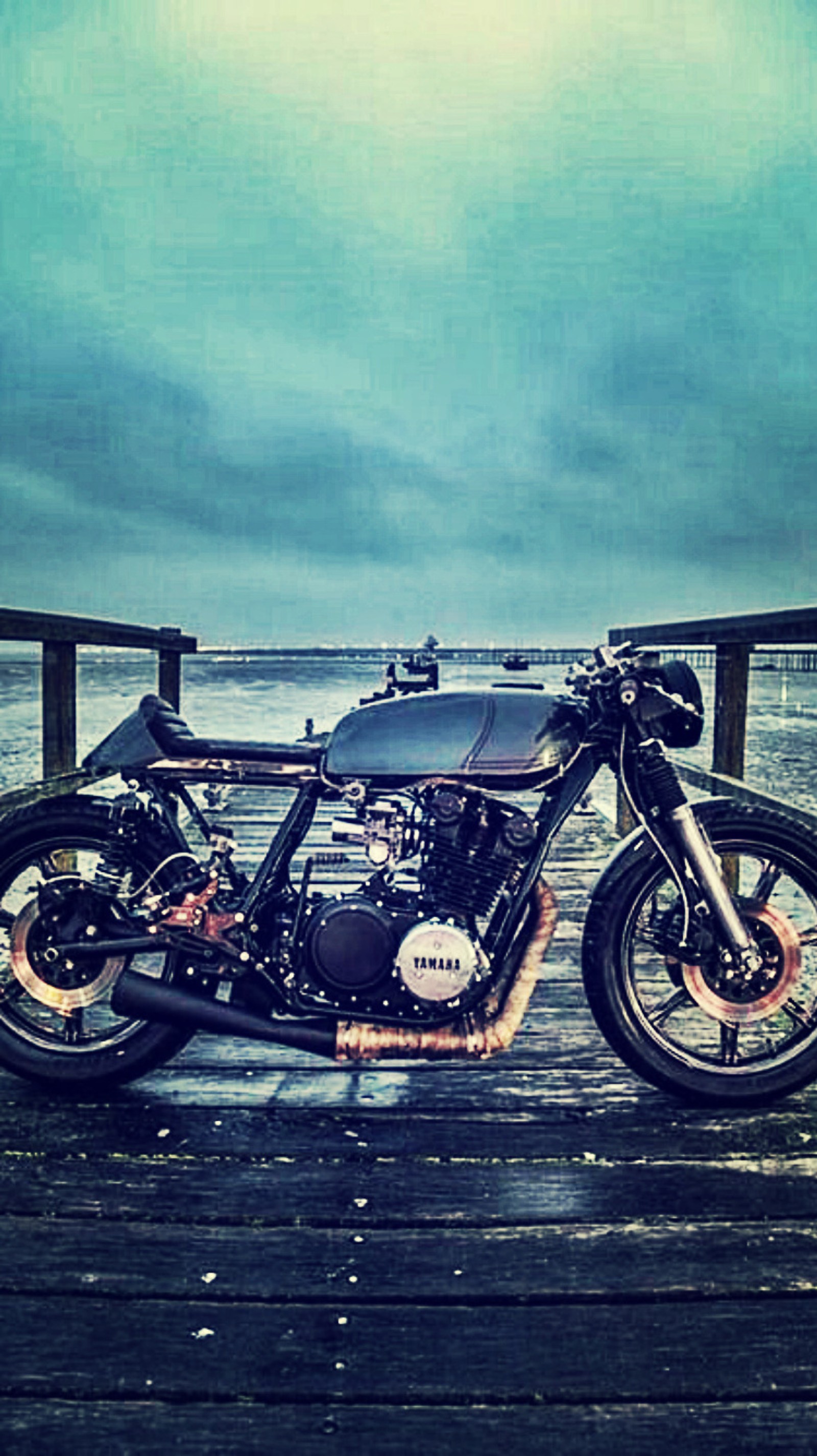 There is a motorcycle that is parked on a wooden dock (cafe racer, moto, yamaha)