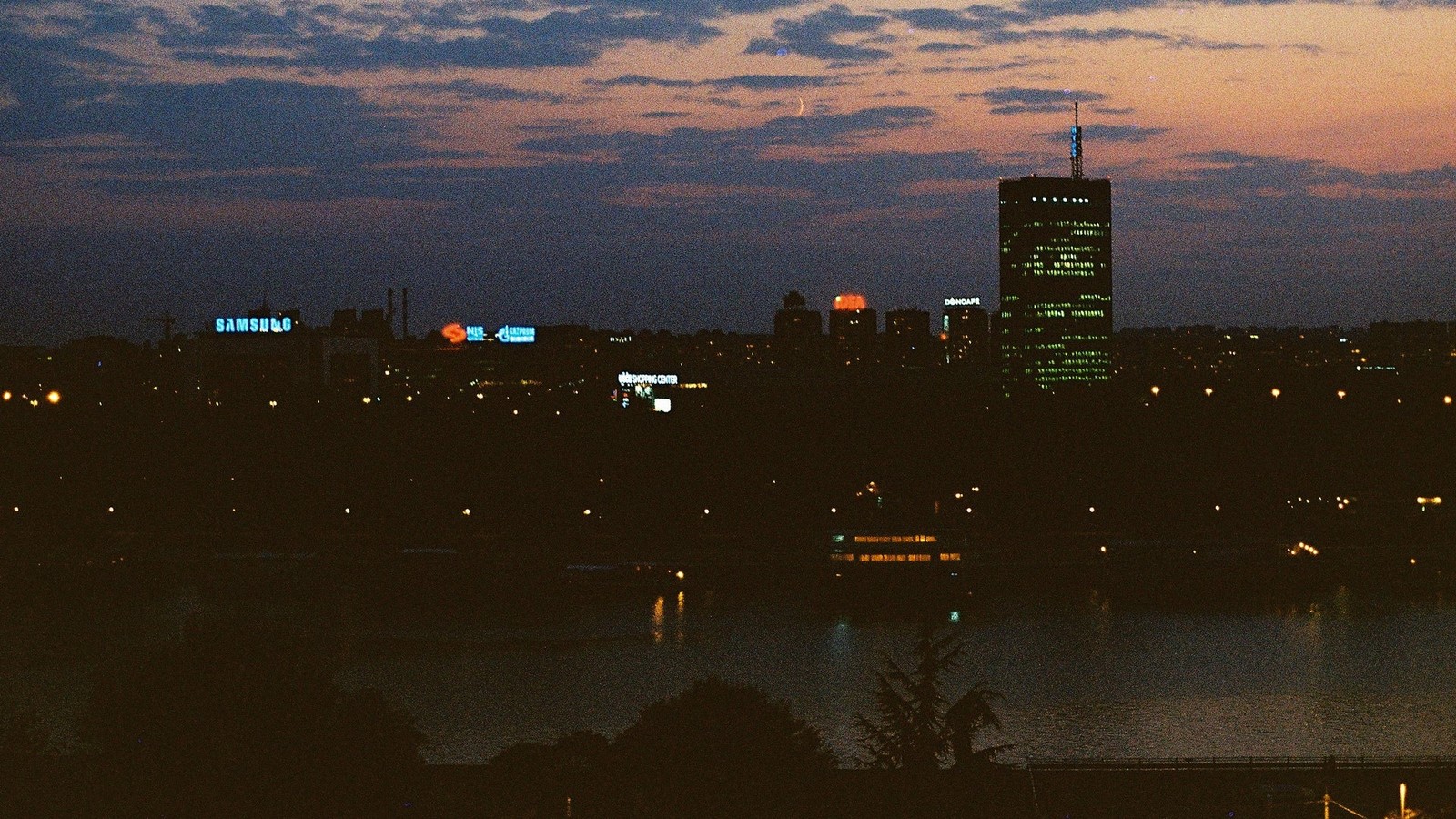 Imagen arafed del horizonte de una ciudad por la noche con un río en primer plano (panorama, nube, edificio, agua, atmósfera)