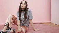 Dua Lipa dans une pose décontractée et stylée devant un fond rose.