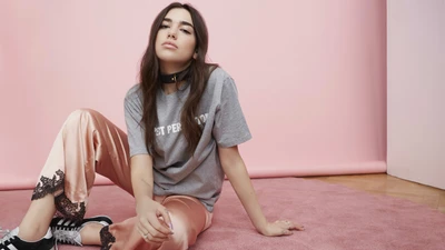 Dua Lipa en una pose casual y elegante contra un fondo rosa.