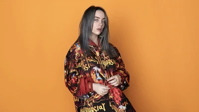 Билли Айлиш в яркой, графической oversized рубашке на оранжевом фоне.