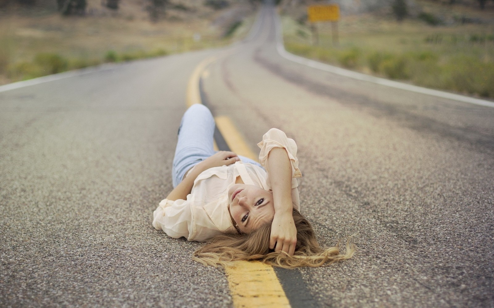 Une femme allongée sur la route avec la tête sur les mains. (route, fille, sable, musique)