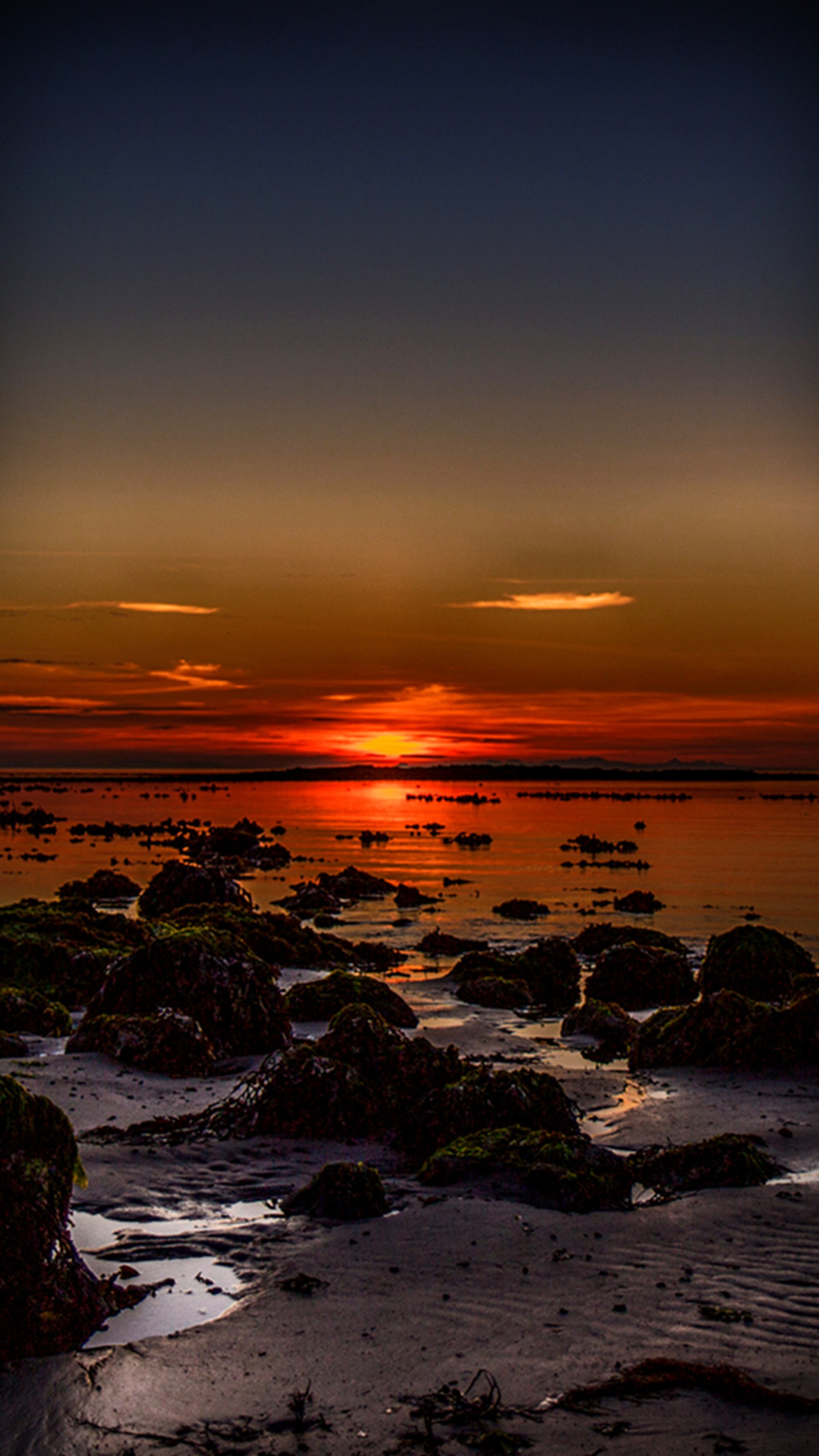 Um pôr do sol na praia com algumas pedras e água (de tirar o fôlego, por do sol)