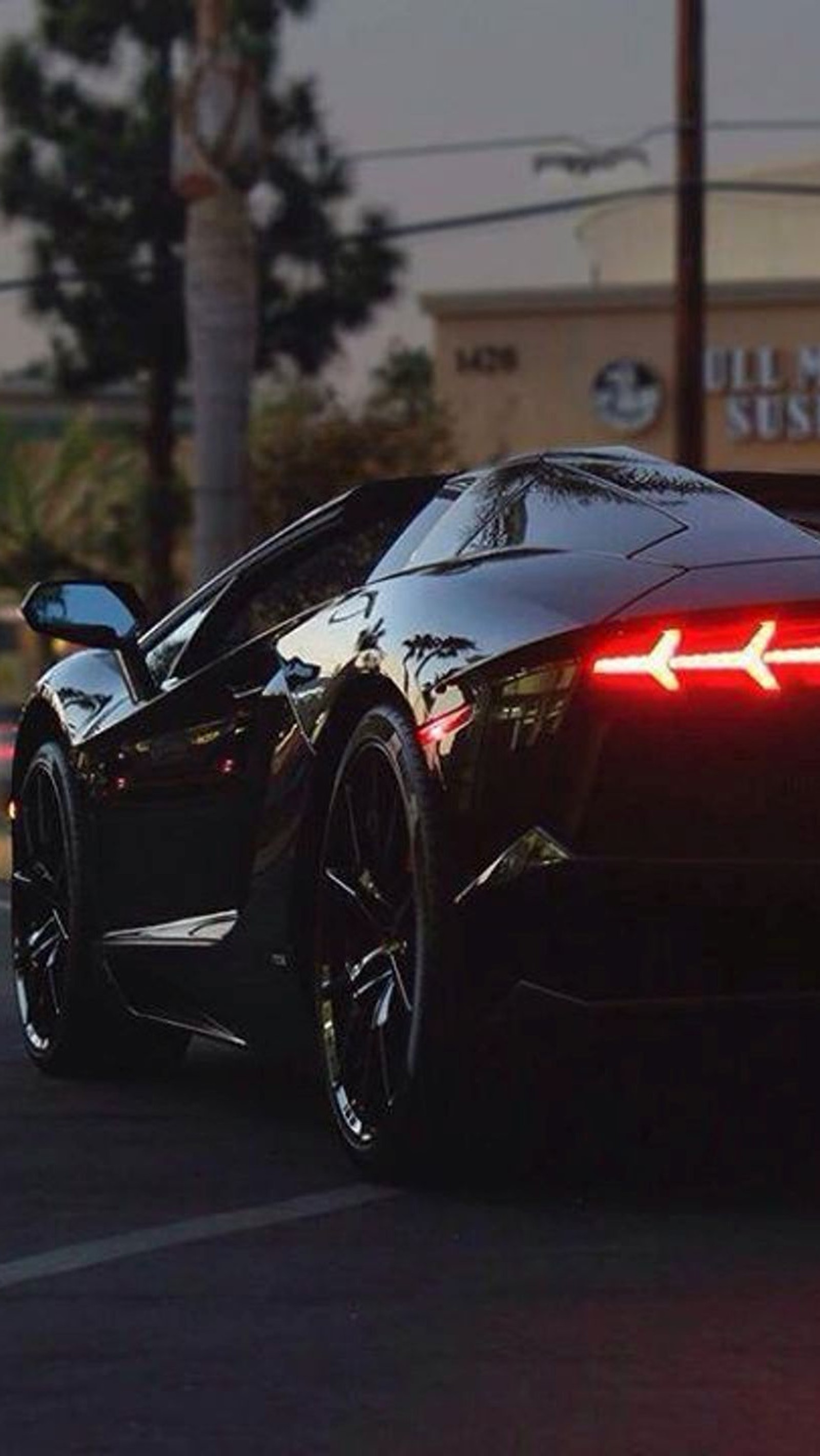 A close up of a black sports car driving down a street (back, car, reventon)