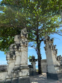 Antike Steinmetzarbeiten, umrahmt von einem hohen Baum in Bali, Indonesien.