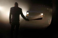 Negan em pé na escuridão nevoenta com um bastão sob a iluminação automotiva